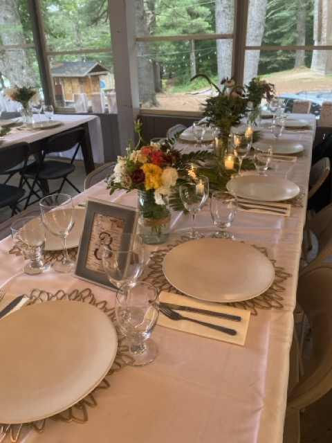 Camp Wigwam dining hall set for a wedding reception with floral centerpieces, candles, gold chargers, and place settings overlooking the pines