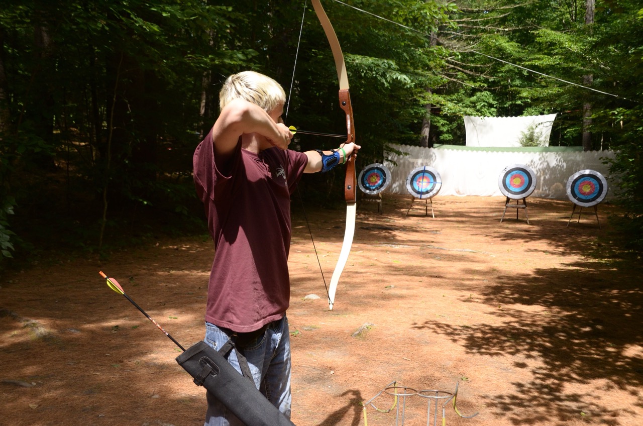Camper drawing back a recurve bow toward bullseye targets at the Camp Wigwam archery range