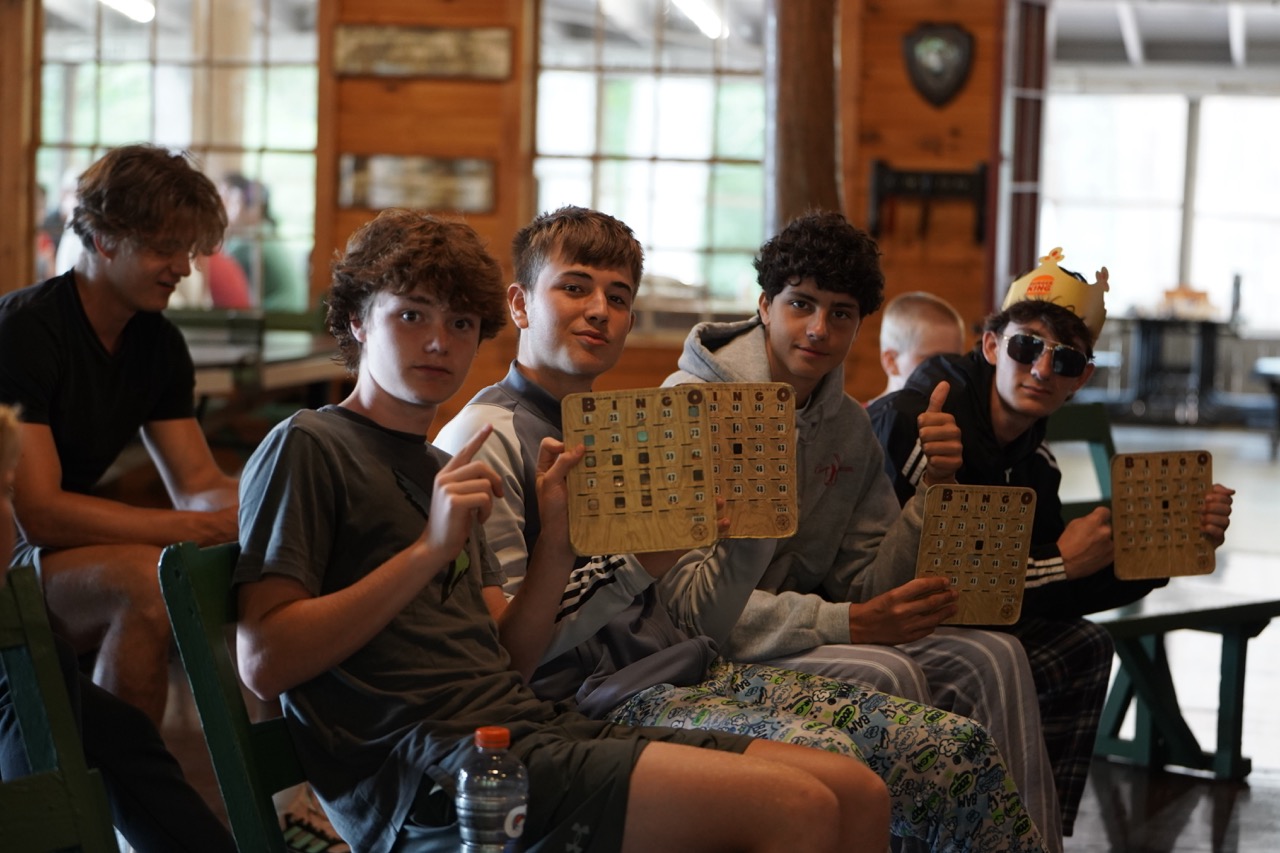 Older campers in the lodge proudly holding up wooden Bingo cards on a rainy day