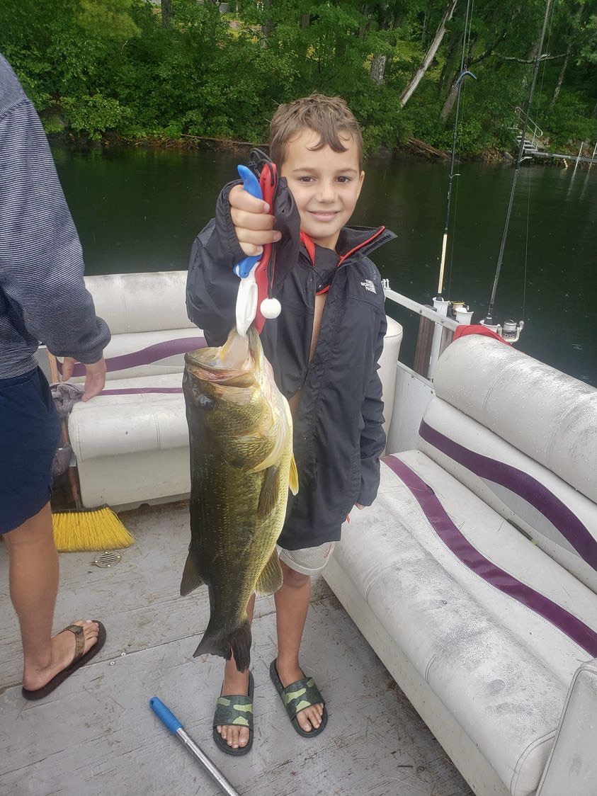 Smiling camper on a pontoon boat proudly holding up a large bass he caught on Bear Lake