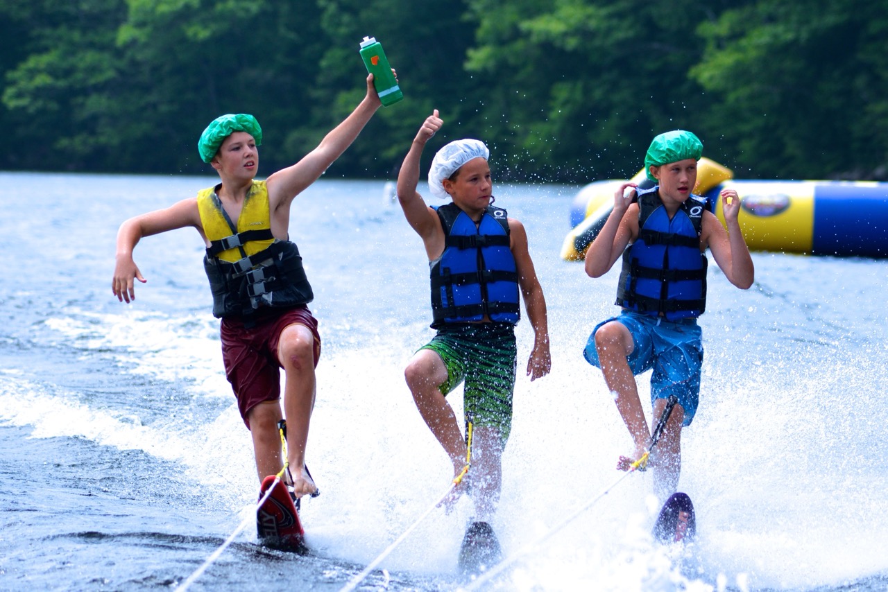 Three campers in life vests barefoot water skiing in a row behind a boat on Bear Lake