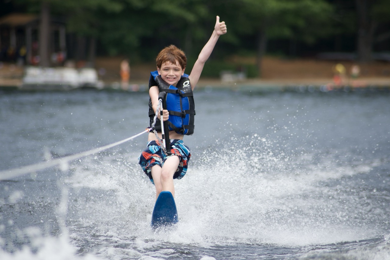 Young camper waterskiing across Bear Lake giving a big thumbs-up to the boat