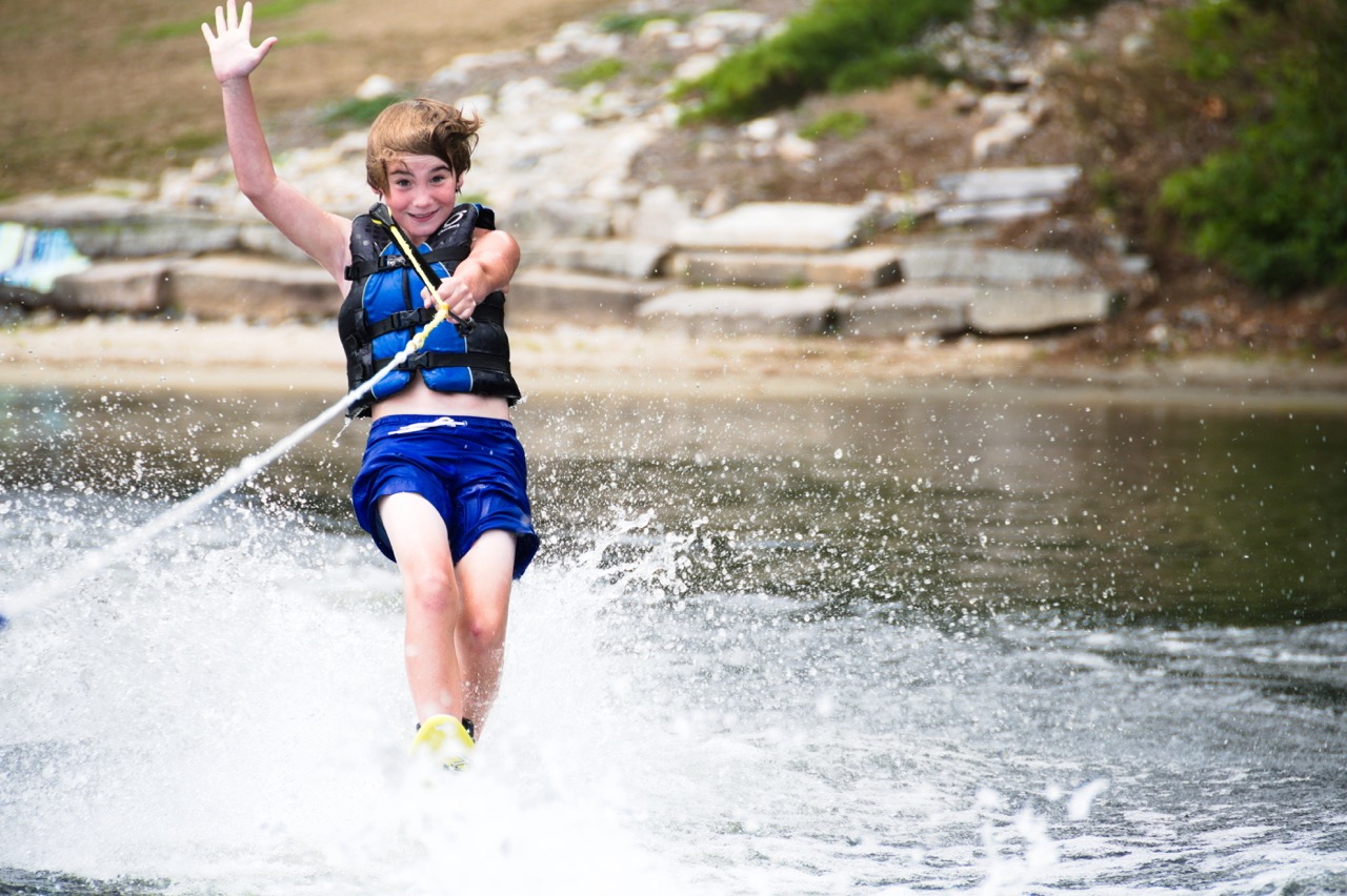 Camper waving while waterskiing past the rocky shoreline of Bear Lake