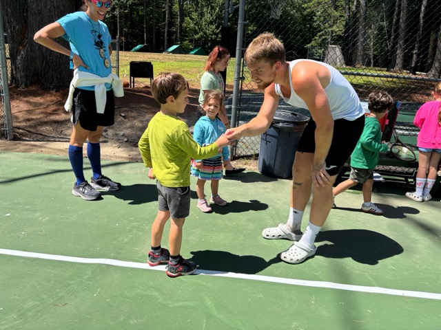 A Little Loon high-fiving a tennis counselor on the courts